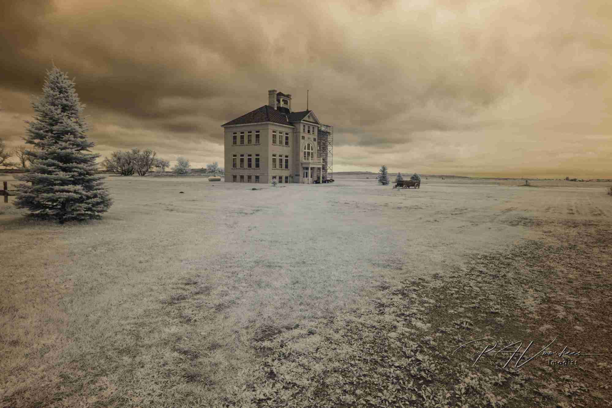 An old two-story schoolhouse alone on the plains under a storm sky, in infrared